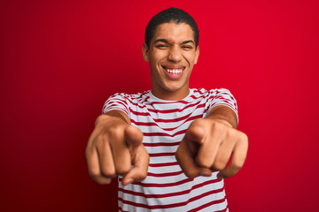 Young handsome arab man wearing striped t-shirt over isolated red background pointing to you and the camera with fingers, smiling positive and cheerful