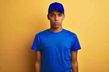 Young handsome arab delivery man standing over isolated yellow background Relaxed with serious expression on face. Simple and natural looking at the camera.