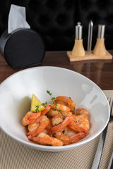 Salad Tiger prawns with lemon, pepper shaker and napkin holder at the table of restaurant close up