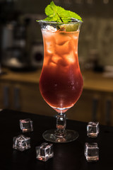 Colorful cocktail in glass on bar counter in pub or restaurant on bright blurred background. A lot of ice cubes and mint