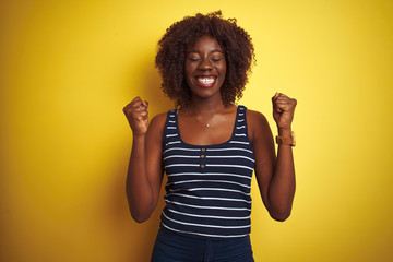 Young african afro woman wearing striped t-shirt over isolated yellow background excited for success with arms raised and eyes closed celebrating victory smiling. Winner concept.