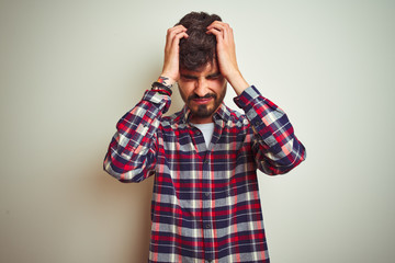 Young man wearing casual shirt standing over isolated white background suffering from headache desperate and stressed because pain and migraine. Hands on head.