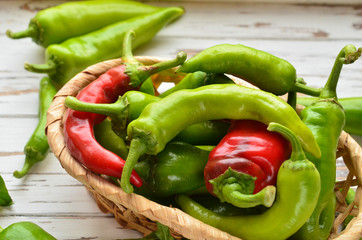 Hot peppers in a wicker basket on a white wooden background.