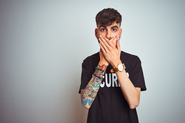 Young safeguard man with tattoo wering security uniform over isolated white background shocked...