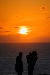Fototapeta premium The silhouette of a family (mother, father and son), watching the sunset (intentionally unfocused), at a cliff by the ocean