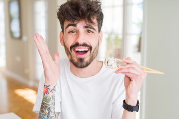 Young man eating asian sushi using chopsticks very happy and excited, winner expression celebrating...