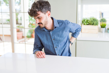 Young man wearing casual shirt sitting on white table Suffering of backache, touching back with hand, muscular pain