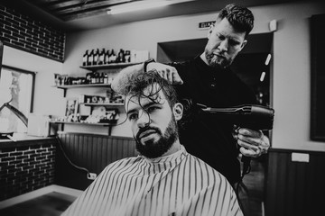 Fototapeta na wymiar Barbershop. Close-up of man haircut, master does the hair styling in barber shop. Strong muscular bearded barber cuts long black hair of the client