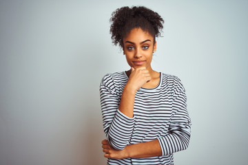 African american woman wearing navy striped t-shirt standing over isolated white background looking confident at the camera smiling with crossed arms and hand raised on chin. Thinking positive.