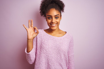 Young african american woman wearing winter sweater standing over isolated pink background smiling positive doing ok sign with hand and fingers. Successful expression.