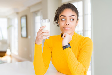 Young african american woman drinking a glass of fresh milk serious face thinking about question,...