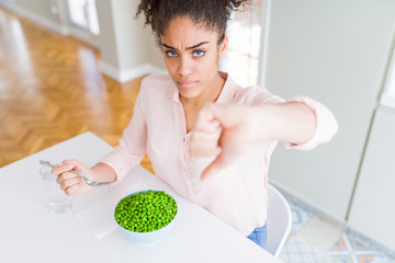Young african american girl eating healthy green peas with angry face, negative sign showing...