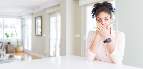 Fototapeta premium Wide angle of beautiful african american woman with afro hair shocked covering mouth with hands for mistake. Secret concept.