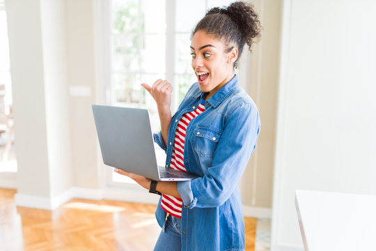 Young african american girl standing working using laptop pointing and showing with thumb up to the side with happy face smiling