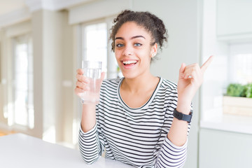 Young african american girl drinking a fresh glass of water very happy pointing with hand and...