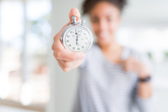 Young african american woman holding stopwatch with surprise face pointing finger to himself