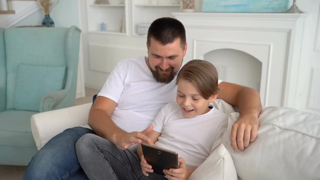 Father and son play together at the tablet and laughing . Family teamwork.