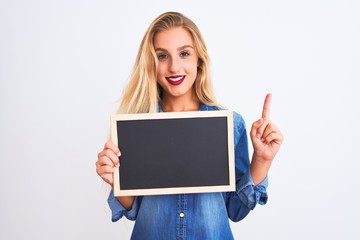 Young beautiful teacher woman holding blackboard standing over isolated white background surprised with an idea or question pointing finger with happy face, number one
