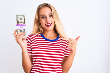 Beautiful woman wearing red striped t-shirt holding dollars over isolated white background happy with big smile doing ok sign, thumb up with fingers, excellent sign