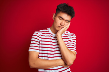 Young asian chinese man wearing striped t-shirt standing over isolated red background thinking...
