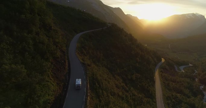 Aerial: Drone approaching towards motor home traveling on winding road over mountains during sunset - Geiranger Fjord, Norway