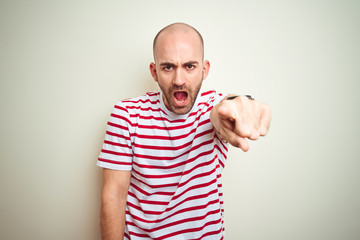 Fototapeta premium Young bald man with beard wearing casual striped red t-shirt over white isolated background pointing displeased and frustrated to the camera, angry and furious with you