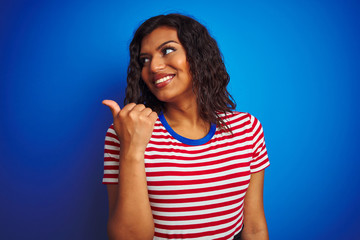 Transsexual transgender woman wearing stiped t-shirt over isolated blue background smiling with happy face looking and pointing to the side with thumb up.