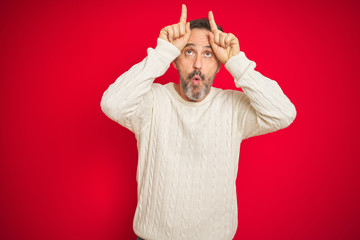 Handsome middle age senior man with grey hair over isolated red background doing funny gesture with finger over head as bull horns