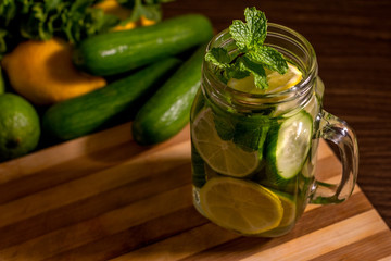 Infused water on a glass surrounded by its ingredients.- Detox water mix of cucumber, lemon, lime...