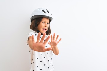 Beautiful child girl wearing security bike helmet standing over isolated white background afraid and terrified with fear expression stop gesture with hands, shouting in shock. Panic concept.