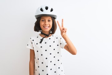 Beautiful child girl wearing security bike helmet standing over isolated white background showing and pointing up with fingers number two while smiling confident and happy.