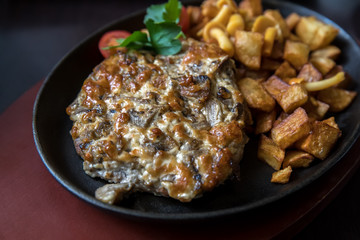 Meat with mushrooms and rustic potatoes on iron pan on a dark background.