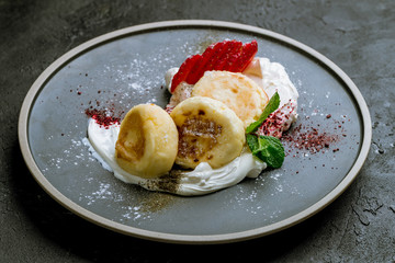 cheesecakes from cottage cheese with strawberry and cream on grey plate on black concrete table