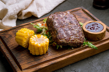 juicy Striploin Steak with pepper, sause and corn on the board on black concrete table