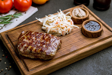 juicy Striploin Steak with sauses and coleslaw on the board on black concrete table