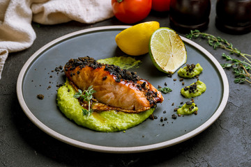 Salmon steak on the grill with lemon and lime on black concrete table