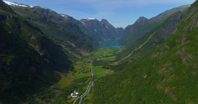 Aerial: Green landscape and lake amidst majestic mountains during sunny day - Briksdal Glacier, Norway