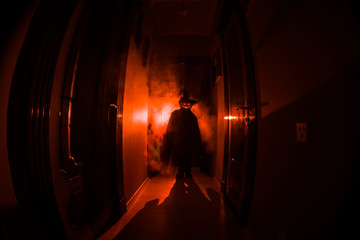 Halloween concept. Creepy silhouette in the dark corridor with pumpkin head. Toned light with fog...