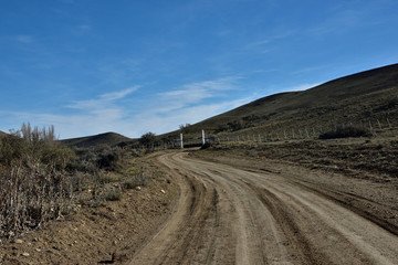 paisaje de camino de tierra con tranquera blanca y cielo azul con nubes