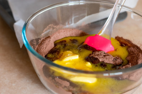 Melted butter being mixed into cocoa powder, sugar and flour with a spatular in a glass bowl.