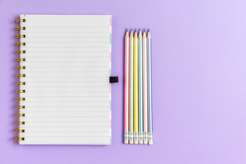 Top view of blank notebook with pencils on purple pastel background, copy space