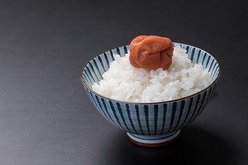 黒背景にお茶碗に白いお米と梅干しがのっているコピースペース
