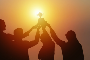 silhouette of  business people holding and raise first place trophy together showing team spirit to win business competition awards