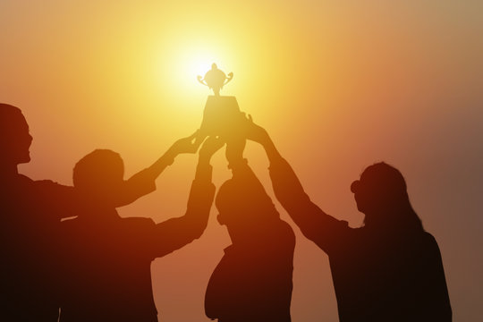 silhouette of  business people holding and raise first place trophy together showing team spirit to win business competition awards