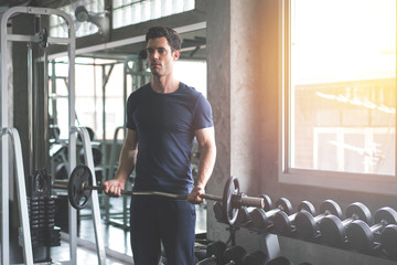 Handsome weightlifter lifting barbells working out with curl bar in the gym