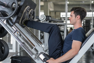 Handsome man lowering weight training legs on leg press machine and working out in the fitness gym