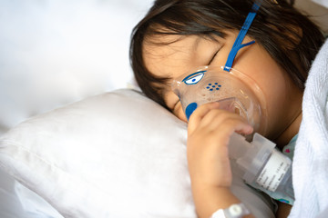 Little Asian girl is sick in a bed with an oxygen mask in hospital