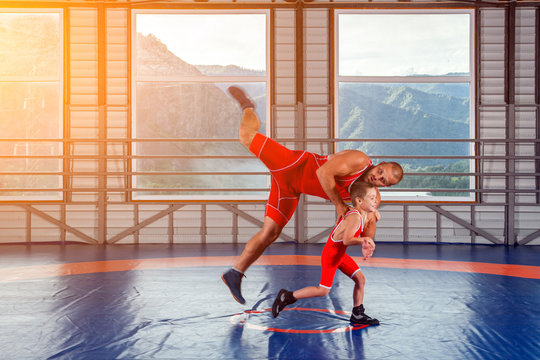 The little boy in sport tights wrestler throws over the hip adult male wrestler on a wrestling carpet in the gym. The concept of child power and martial arts training. 