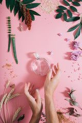 Transparent perfume bottle in flowers on pink background with woman's hands. Spring background with...