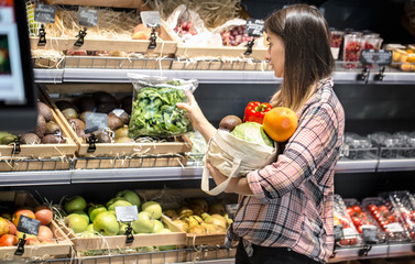 A young girl chooses fruits and vegetables in the store and puts them in eco bag